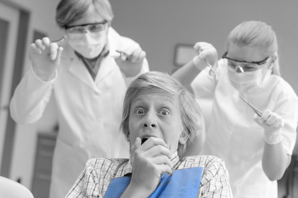 Person holding mouth as dentist and assistant sneak up behind.